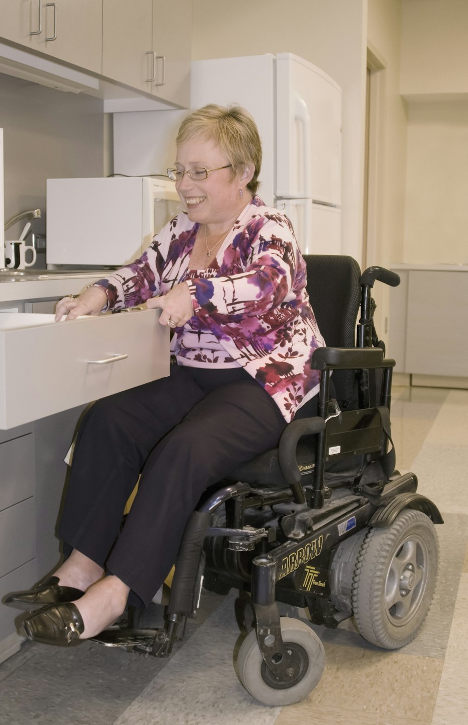Femme en fauteuil roulant électrique accédant à un tiroir de cuisine adapté.